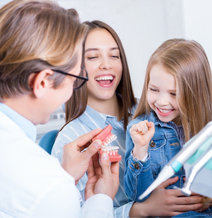 Mother and daughter at orthodontic office. Daughter is engaged in laughter as orthodontist uses humor by playing with a fake set of teeth.