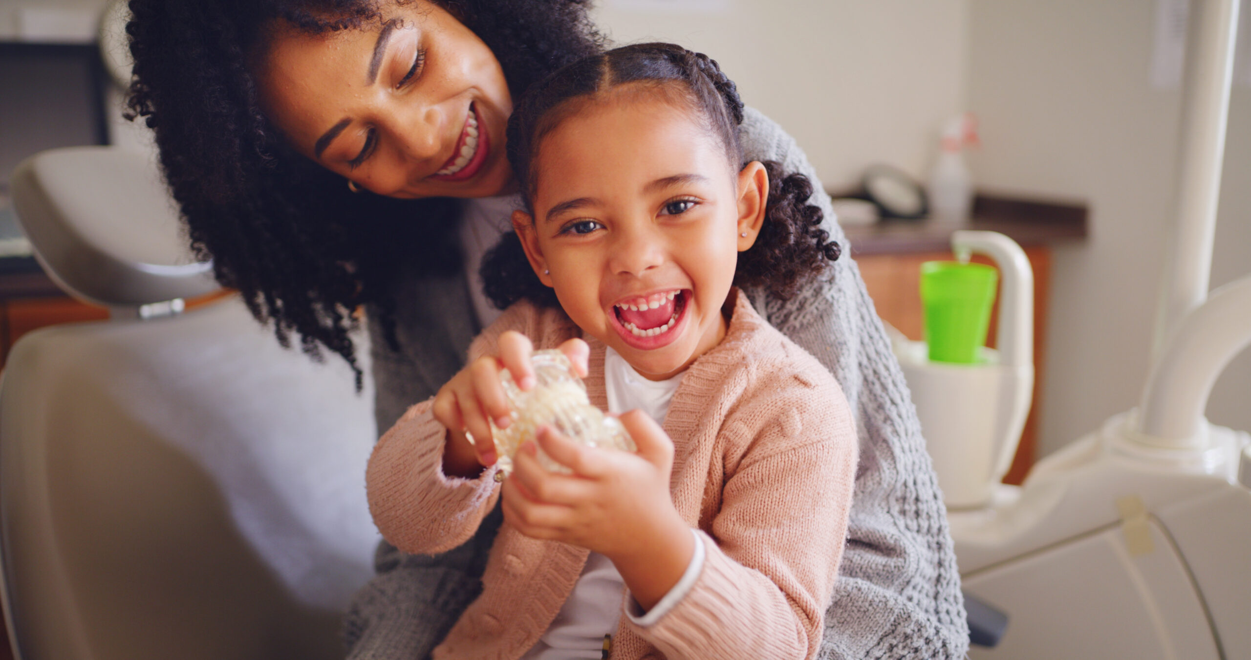 Happy child, mother and tooth model at dentist office for learning oral health, play and excited. Mom, girl and pediatric orthodontics with teeth, typodont and dental care with parent for portrait